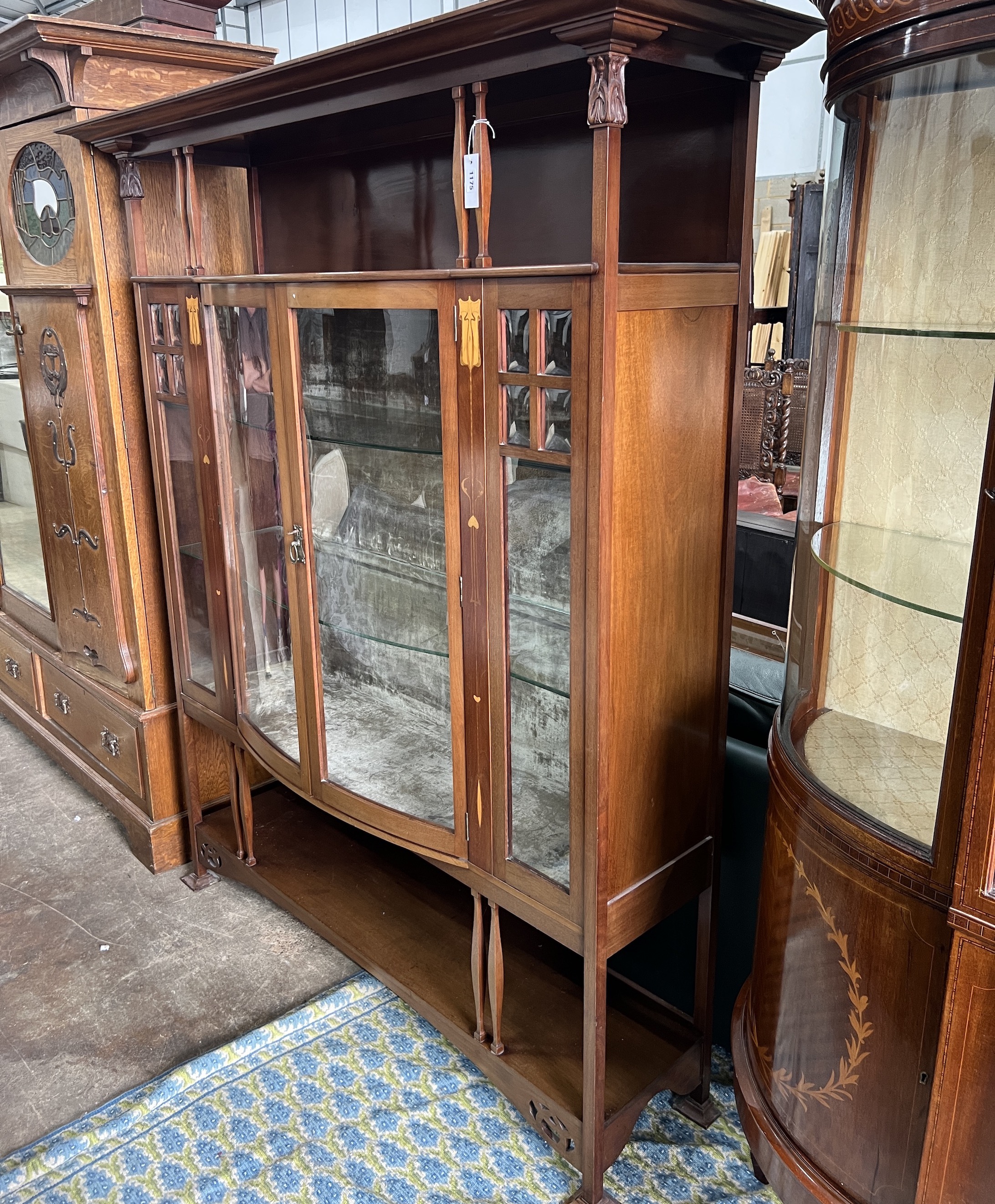 An Arts & Crafts marquetry inlaid mahogany bowfront display cabinet, width 157cm, depth 38cm, height 183cm